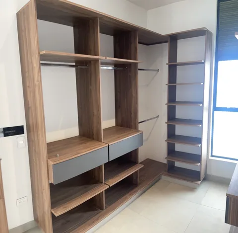 Módulo de closet con barra, cajones y repisas en tono madera, junto a una ventana