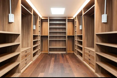 Walking closet instalado con barras, cajoneras y repisas en tono madera, piso de madera y luz natural