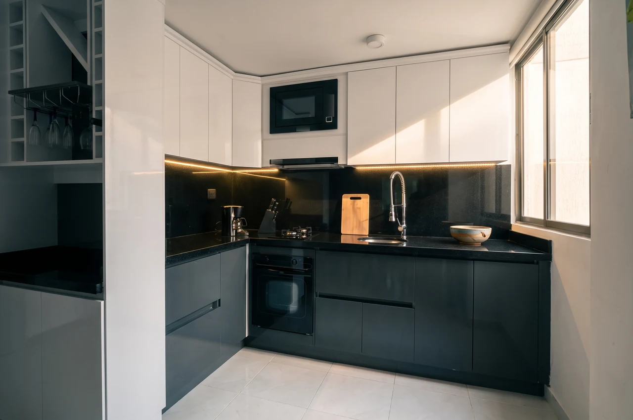 Cocina minimalista en blanco y gris grafito, con frentes lisos sin manijas, fogón empotrado y salpicadero oscuro