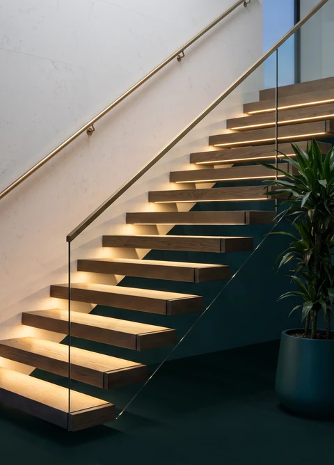 Escalera flotante en madera con baranda de vidrio y pasamanos, iluminada
